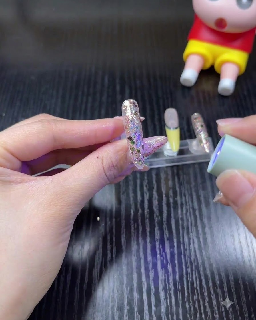 グリッターネイルの上に小型のハンディUV/LEDランプをかざしてジェルを硬化させている手。