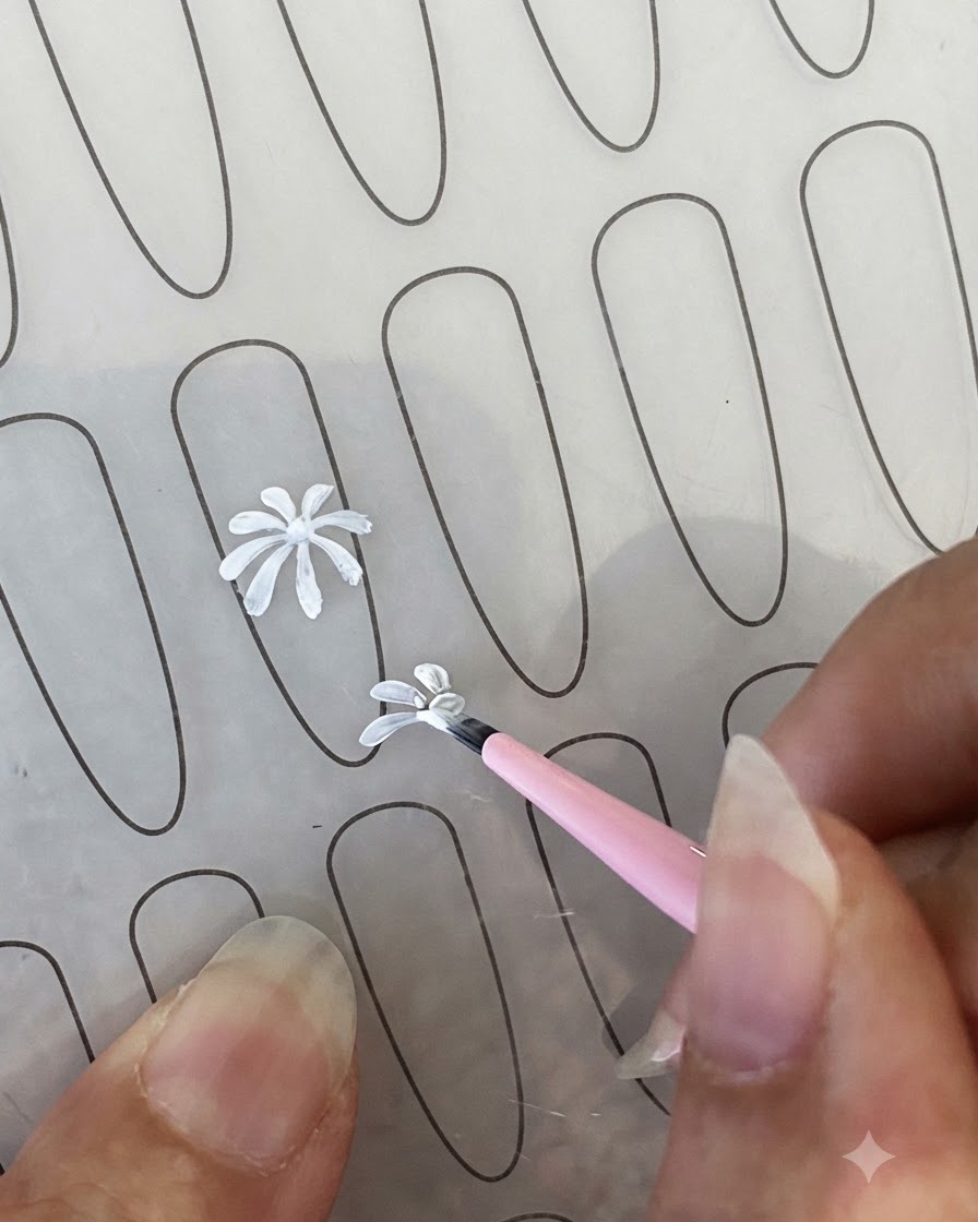 練習用のネイルシート上に描かれた、最初の白いデイジーの花びらの輪郭と、その隣にある極細ライナーブラシ。