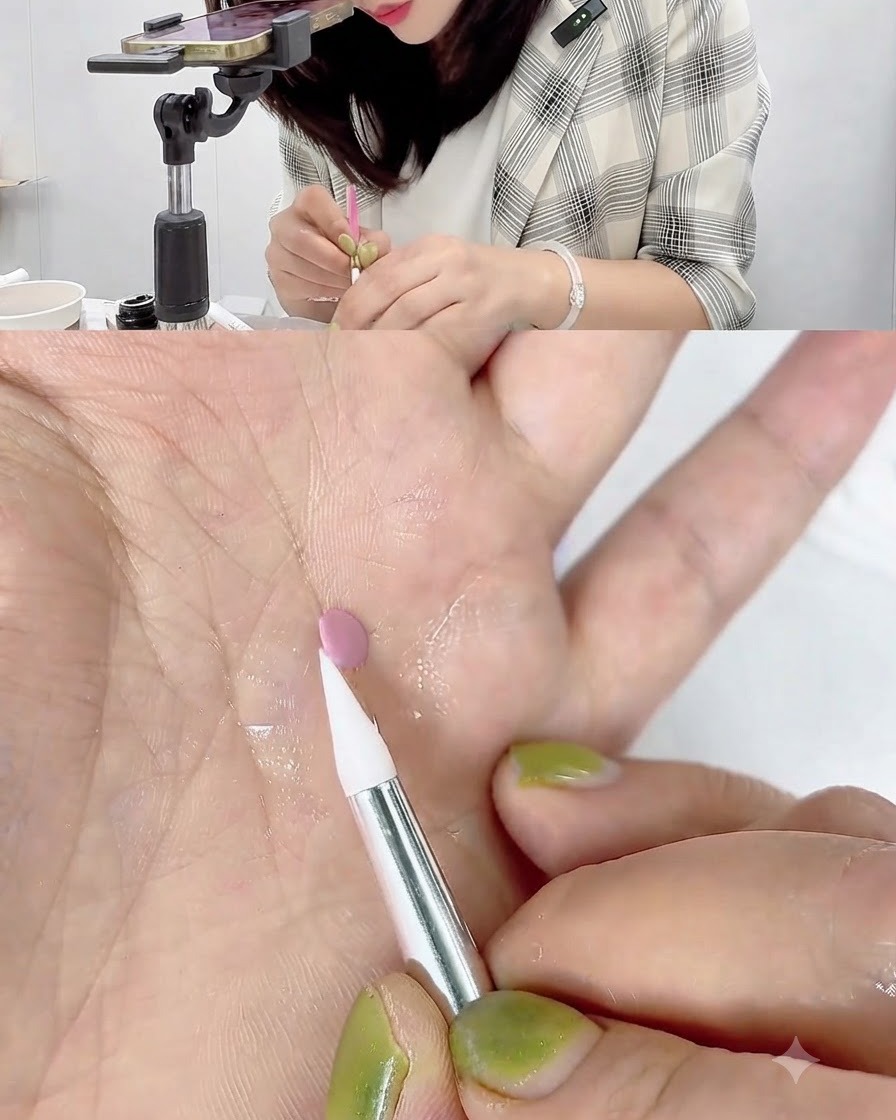 手のひらの上で、白いシリコンカービングペンが小さなピンクのジェル円盤の端に触れて丸めている様子。
