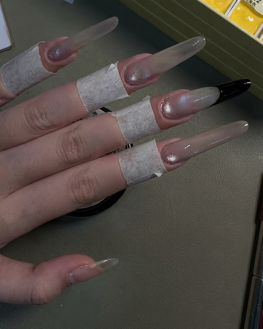 真珠光沢のあるグレーのキャッツアイシマーで仕上げられた4本のロングスティレットネイルを見せている手。