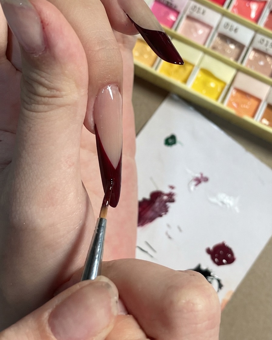 黒のフレンチチップの上に、小さなダークプラムのアクセントや花びらの形を書き加えている細いブラシ。