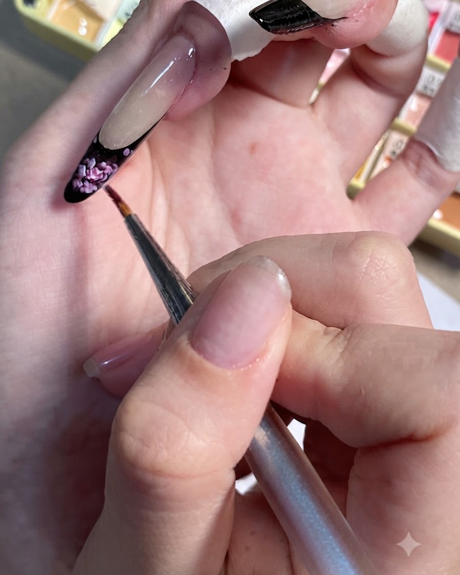 ペイントされたネイルの黒のフレンチチップに、小さなライトピンクのアクセントをドット状に置いているディテールブラシ。