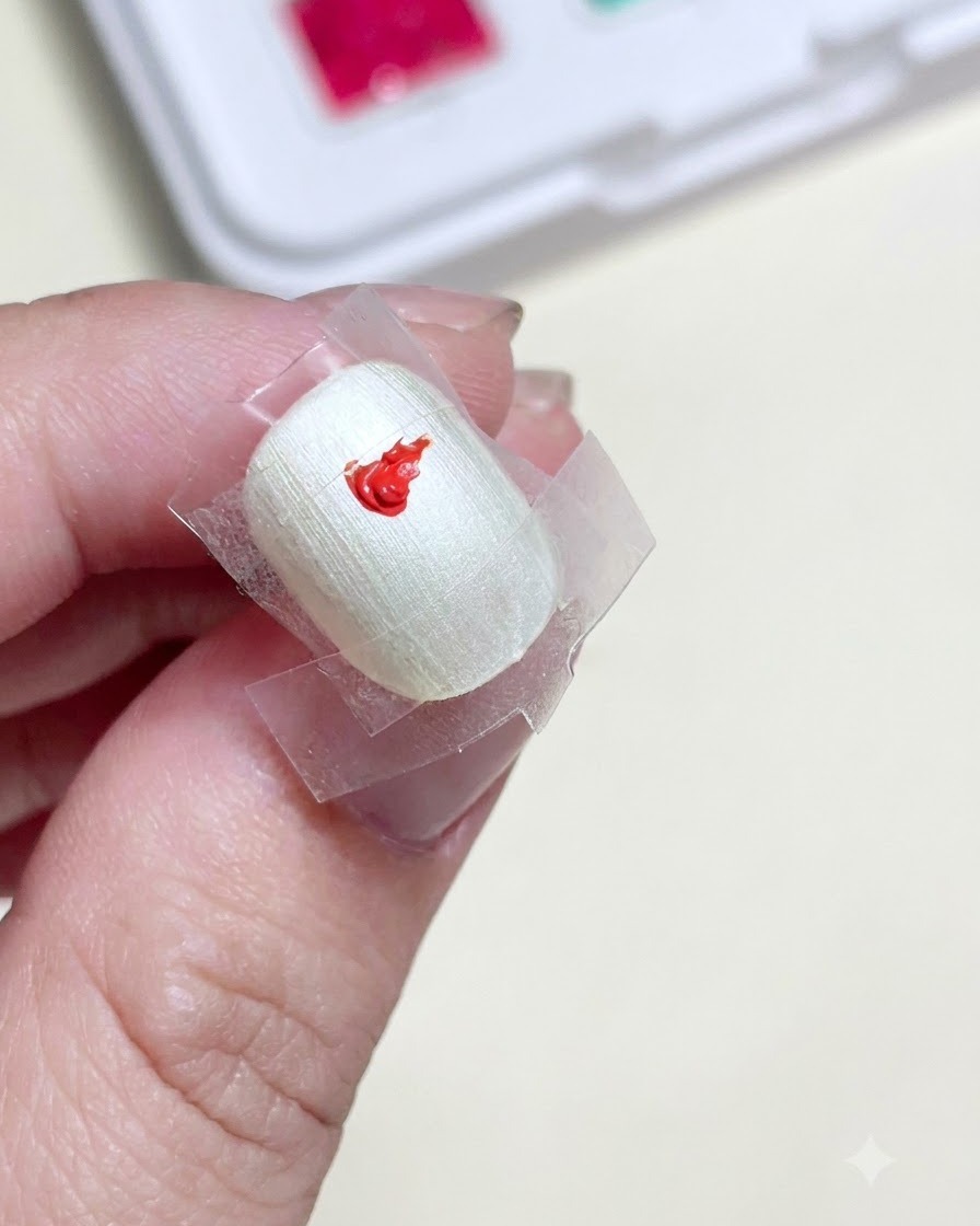 中央にクリアテープの正方形がある下処理済みの爪に、鮮やかな赤のジェルペイントのドットが置かれているクローズアップ。