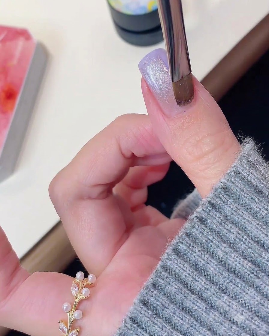 パープルに輝くキャッツアイジェルの爪の上にマグネットツールをかざしている様子。
