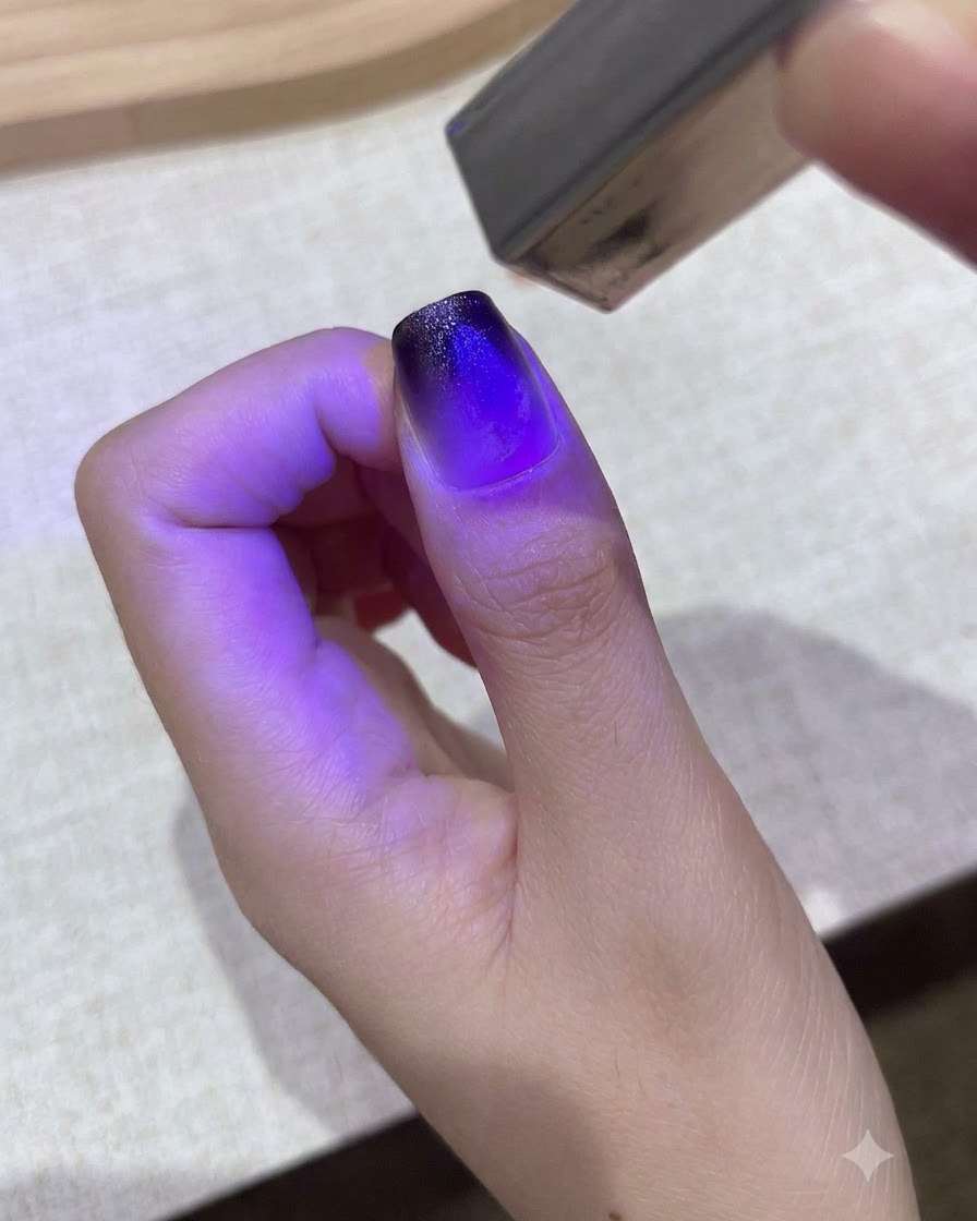 小さな紫色のハンディUV/LEDランプが親指のグラデーションジェルデザインを硬化させている様子。