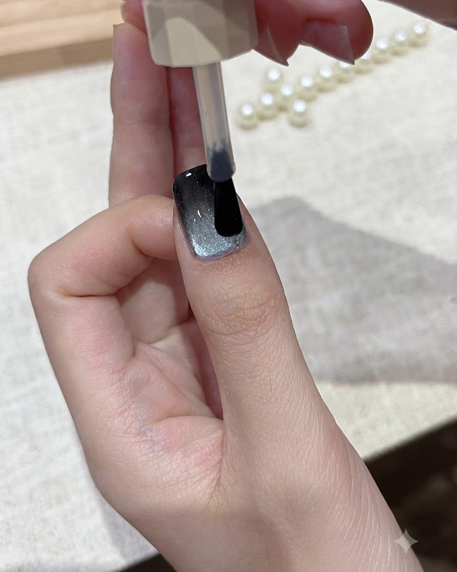 ブラシが仕上げのキャッツアイネイルデザインの上にクリアなグロッシートップコートの層を滑らせている様子。