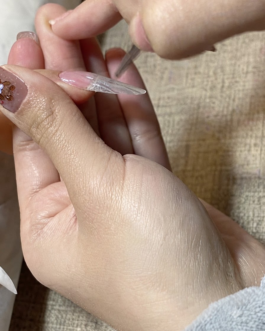 細筆を使って、ネイルエクステンションの表面にのせたクリアジェルをなめらかに整えているクローズアップ画像。