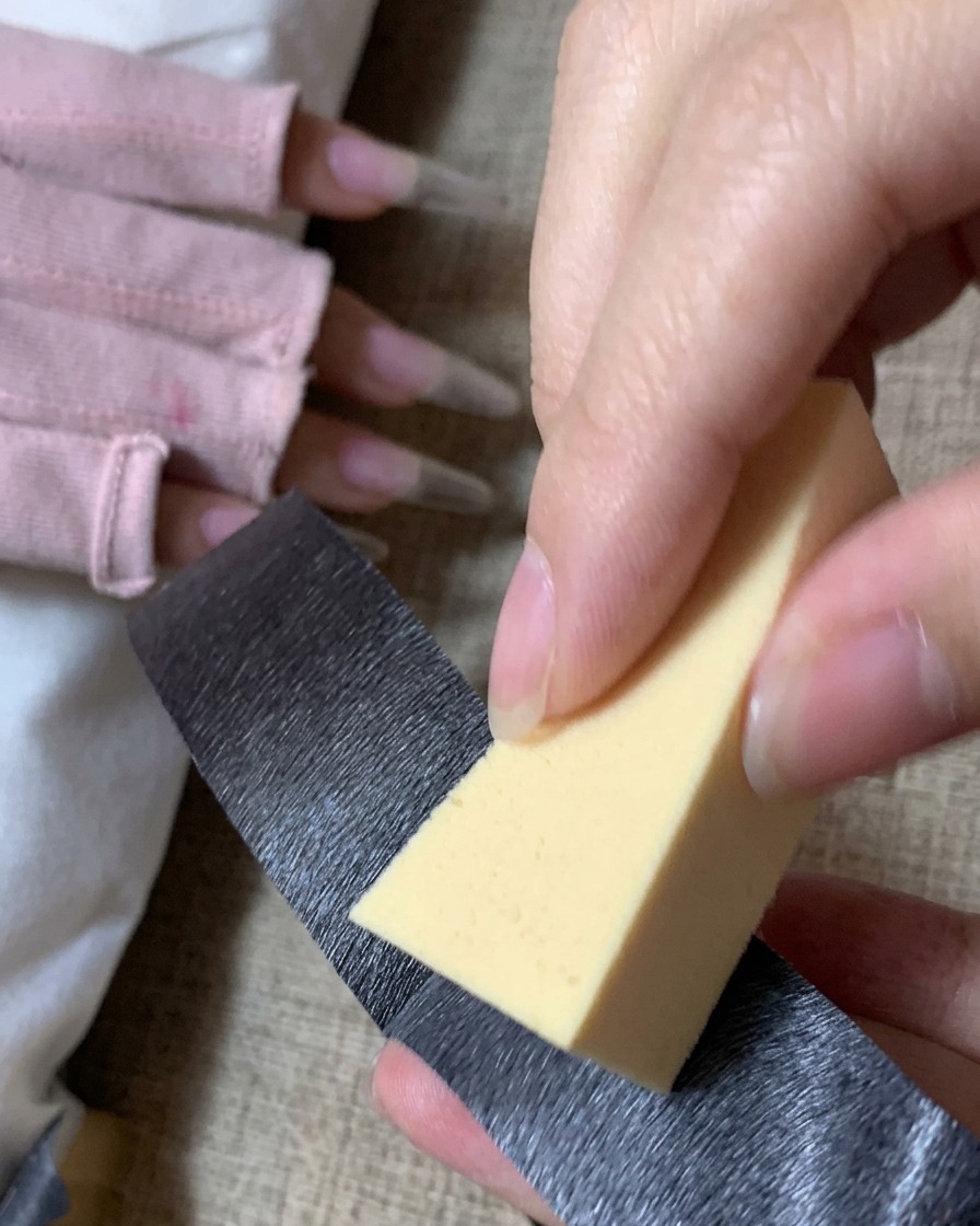 黒い粘着テープを使って、黄色い三角形のメイク用スポンジからホコリを取り除いている様子。