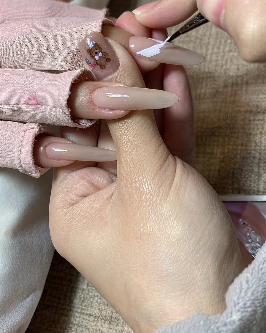 長い爪に描かれた白い蝶の羽の模様を、ネイルアーティストが細かく調整している様子。