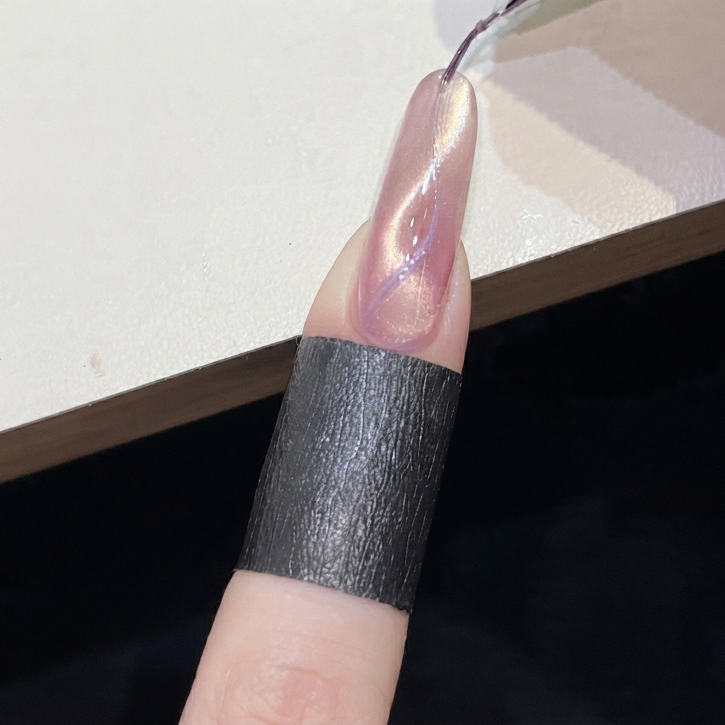 ピンクのきらめくネイル上に描かれたパープルのキャッツアイラインの近くで、円柱型マグネットを操作しているところ。