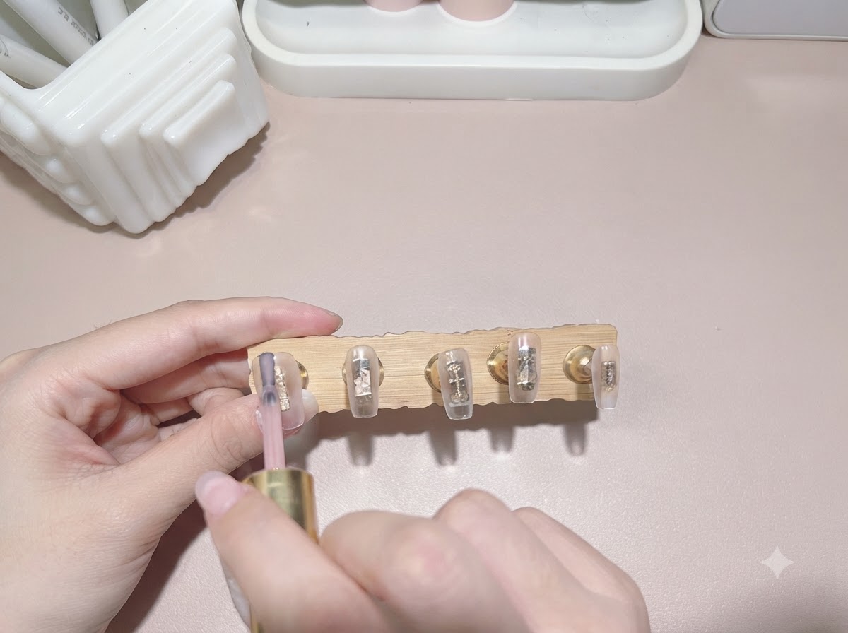 ネイルチップに透明感のあるミルクティーカラーのジェルを筆で塗布している様子。