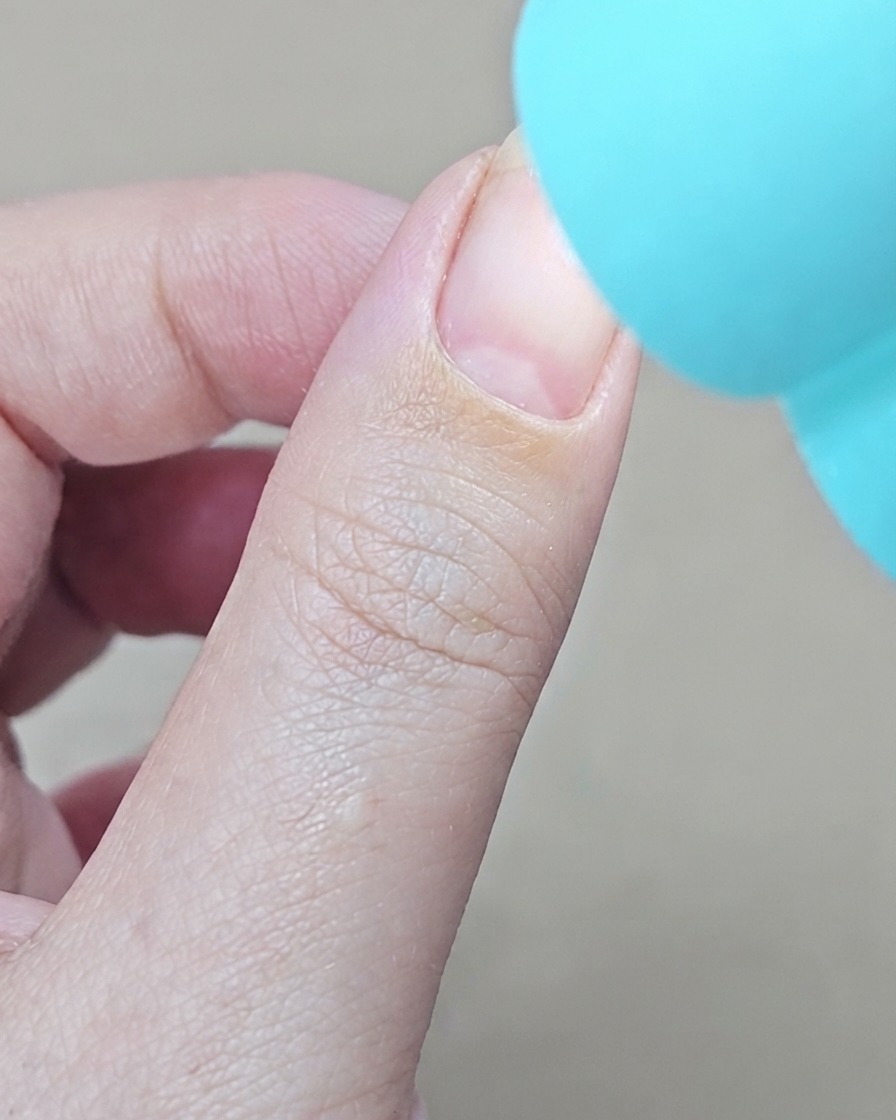 青い光を放つ小型ハンディUV/LEDライトを指の上に当てて硬化している様子。