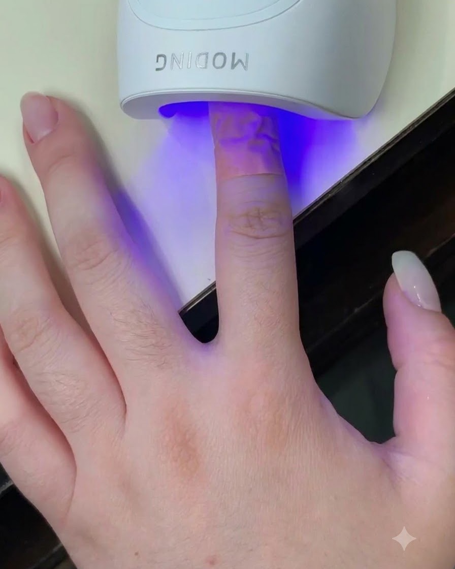 青い光が爪に当たっている白いミニUV LED硬化ランプの中に置かれた指。
