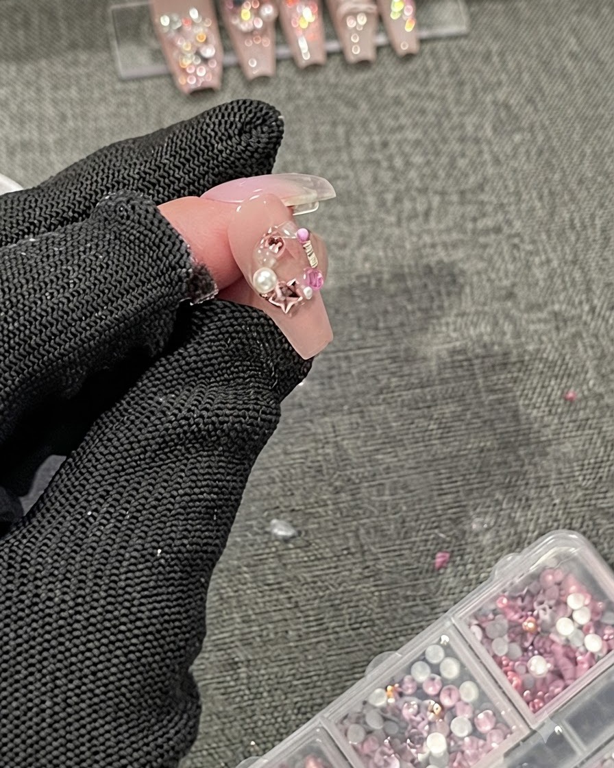 細部用ブラシが、3Dネイルチャームやラインストーンの端の周りにトップコートのシーラントを塗布している様子。