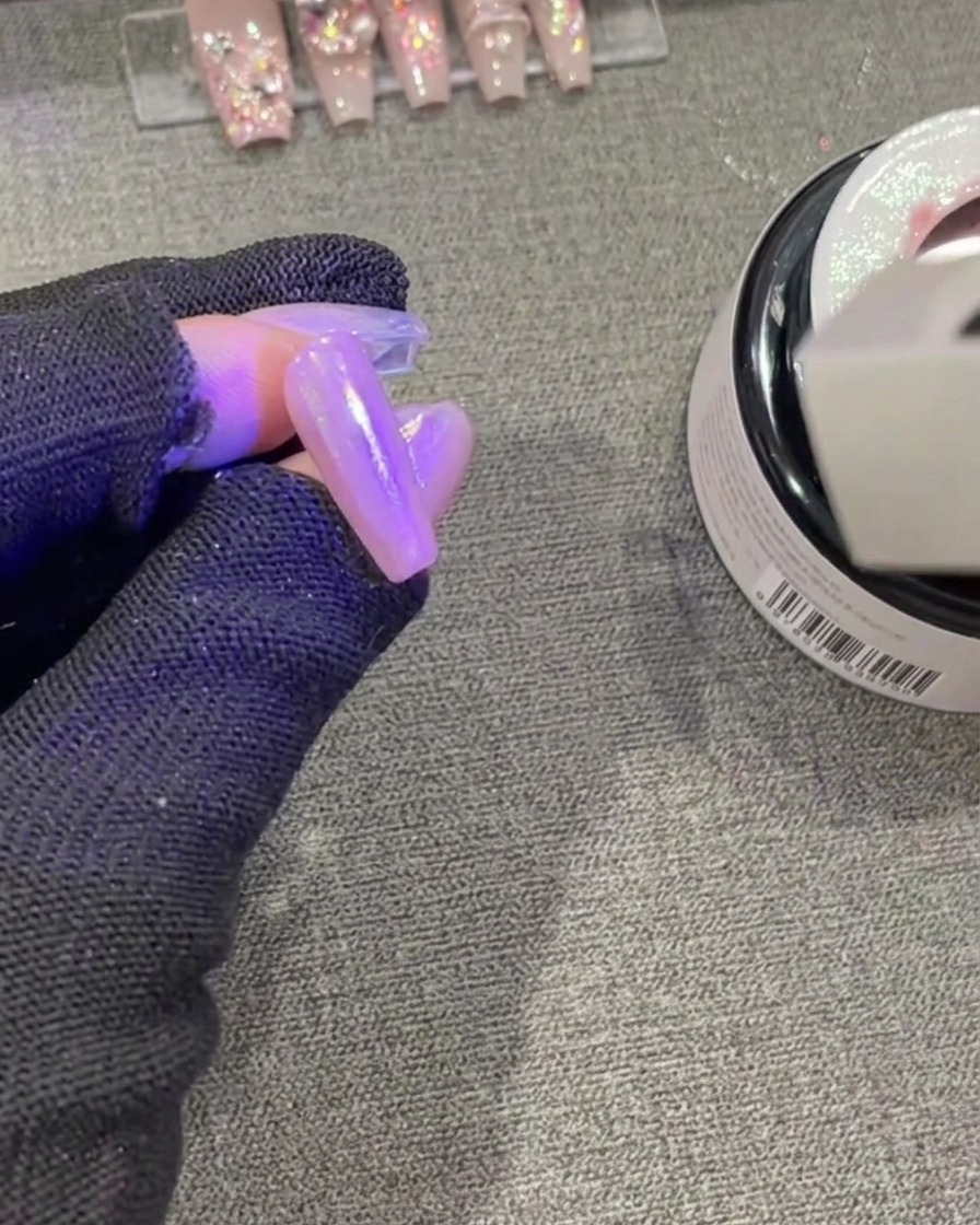 濡れたジェルが光を反射しながら、紫色のUV/LED硬化ランプの下で照らされているネイル。