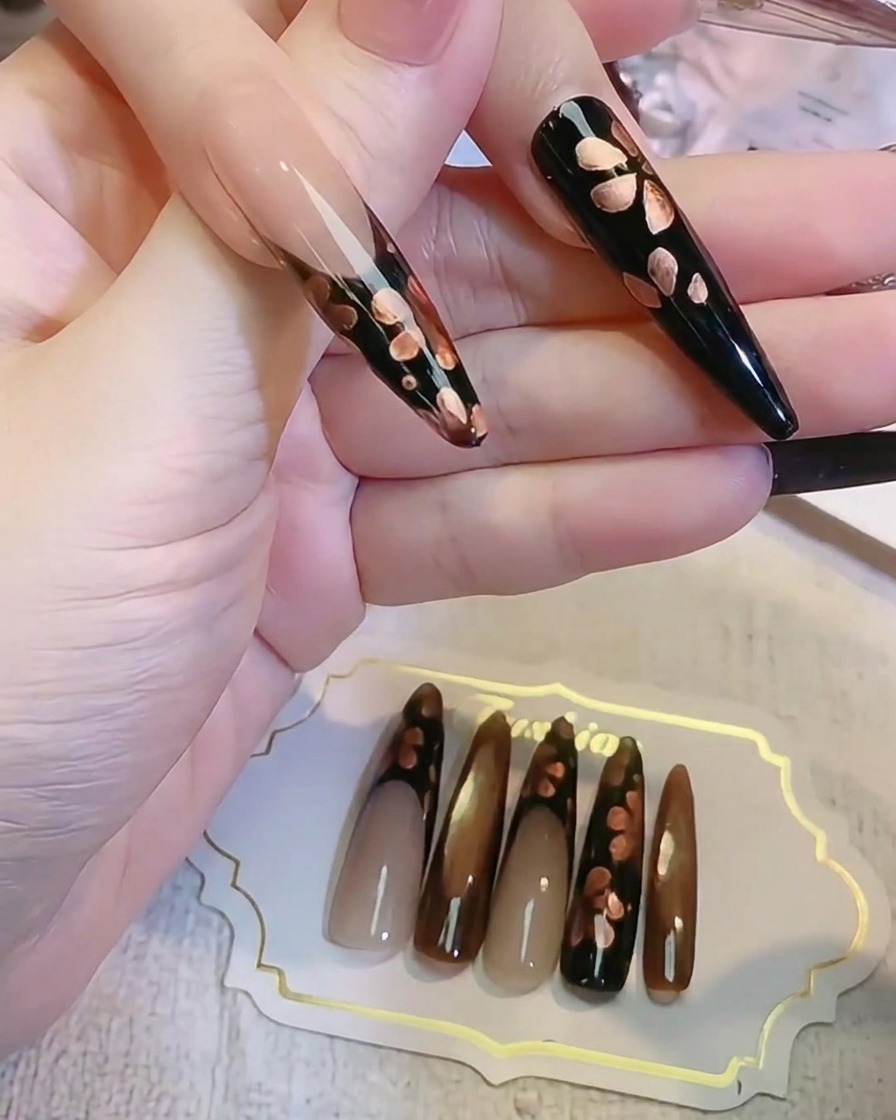 細いライナーブラシでダークな黒いネイル表面にメタリックブロンズの花びらのディテールを描いている様子。