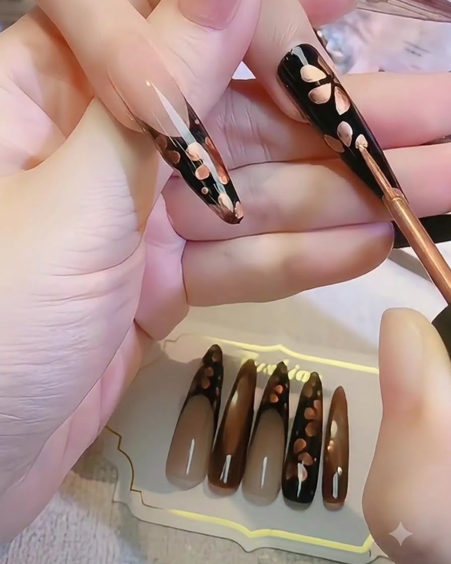 黒いネイル上で細いブラシを使い、ブルーミングするメタリックな花の形を作成しているクローズアップ。