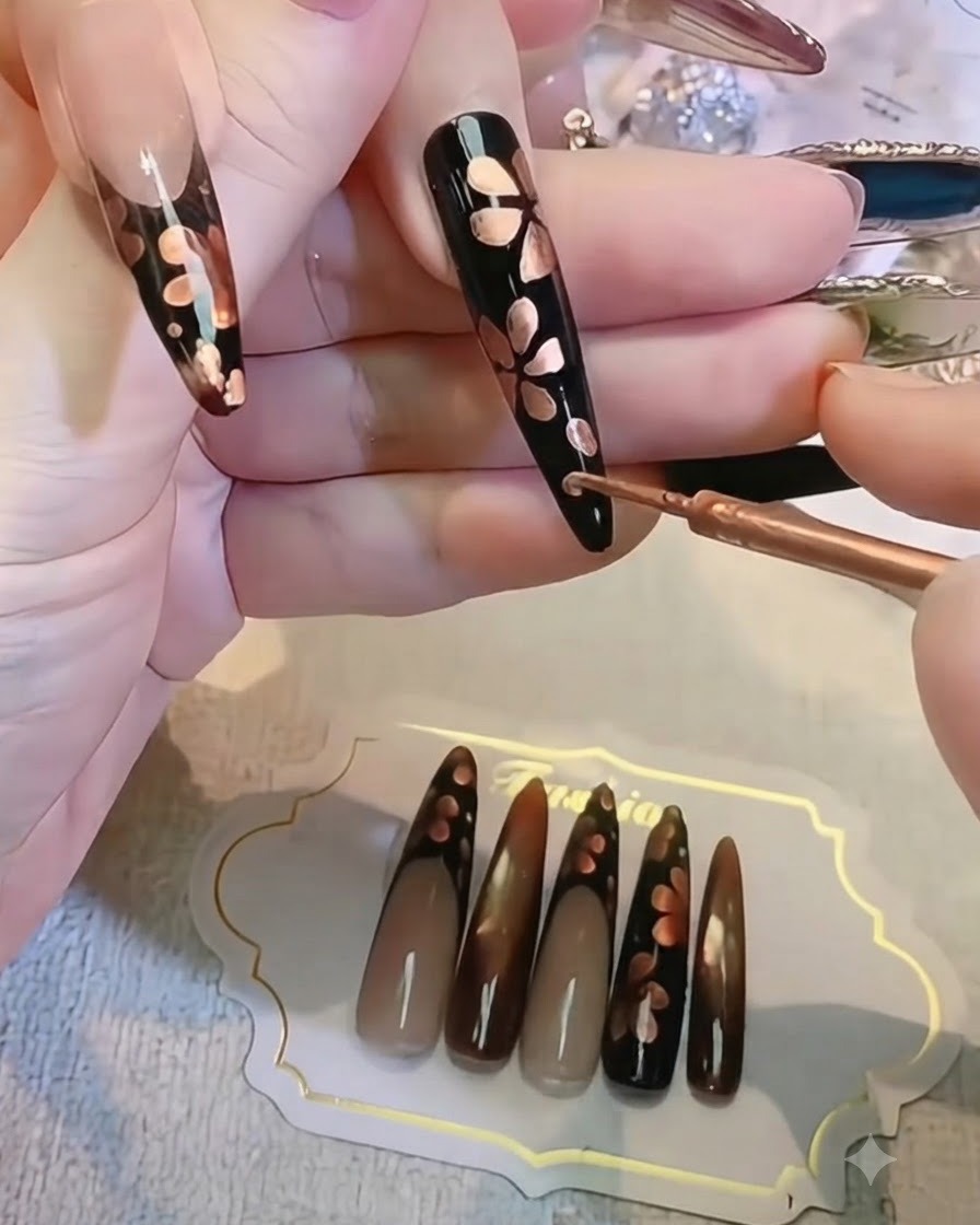 長い黒いネイル上で、細いブラシを持ってフローラルウォーターカラーのディテールを整えている手。