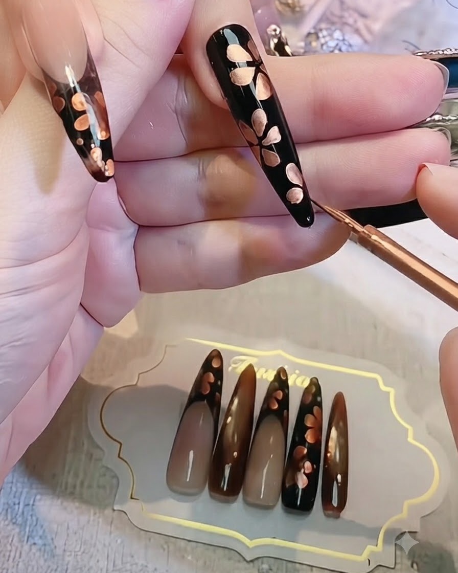 完成した黒とブロンズのフラワーネイルデザインを指の上で間近にチェックしている様子。