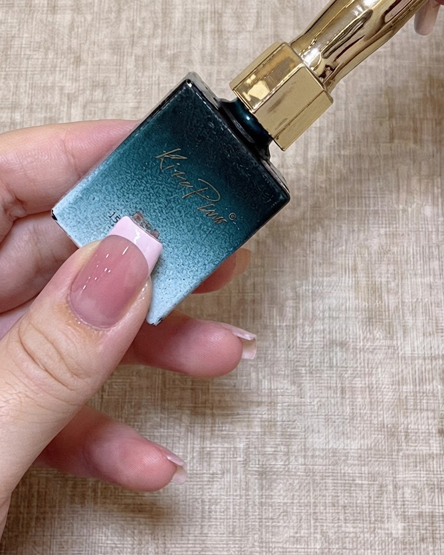 細いネイルブラシが、くすみピンク（ビーンペースト）カラーのジェルポリッシュのボトルに浸されているクローズアップショット。