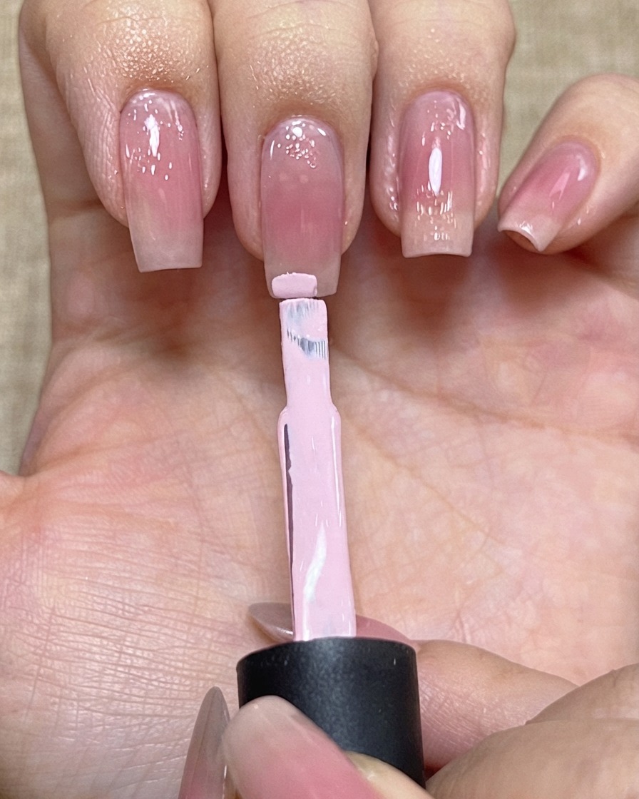 ライトピンクのジェルを載せたネイルポリッシュブラシが、爪のエッジ付近に位置している様子。