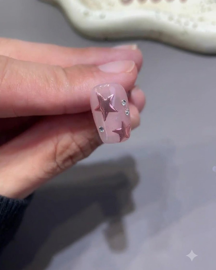 完成したピンクスターのネイルにある小さなラインストーンのベースの周囲に、小さなディテールブラシでトップコートを細かくペイントしている様子。