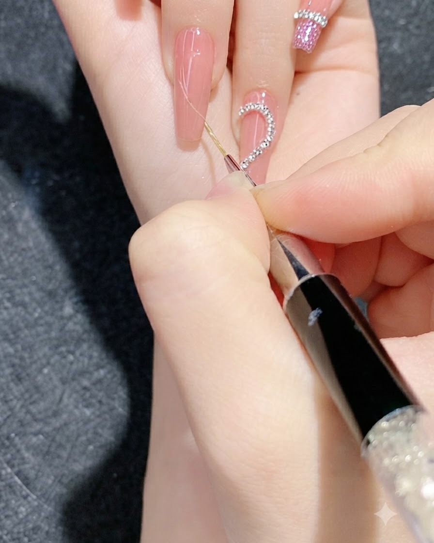 細かいツールを使い、グラデーションを施した爪の上のデザインラインに沿ってラインストーンチェーンを押し込んでいるクローズアップ画像。