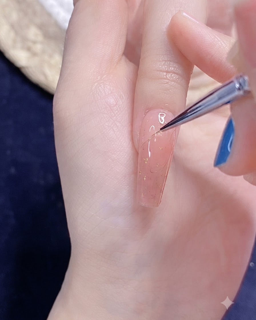 ピンク色に塗られた爪の上で、極細のネイルアートブラシを使用して繊細な半分のハートのアウトラインを描いている様子。