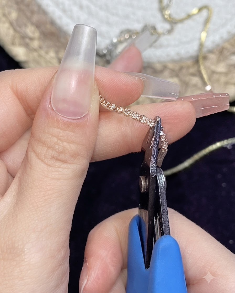 指の間で挟んだゴールドのメタルチェーンストリップを小型のニッパーで切り取っている様子。