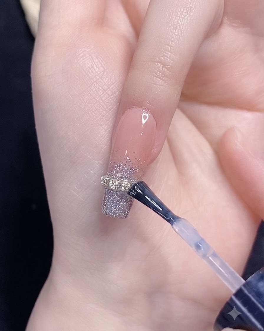 チェーンストリップのアクセントがあるシルバーグリッターのグラデーションネイルに、ブラシでトップコートを塗布している様子。