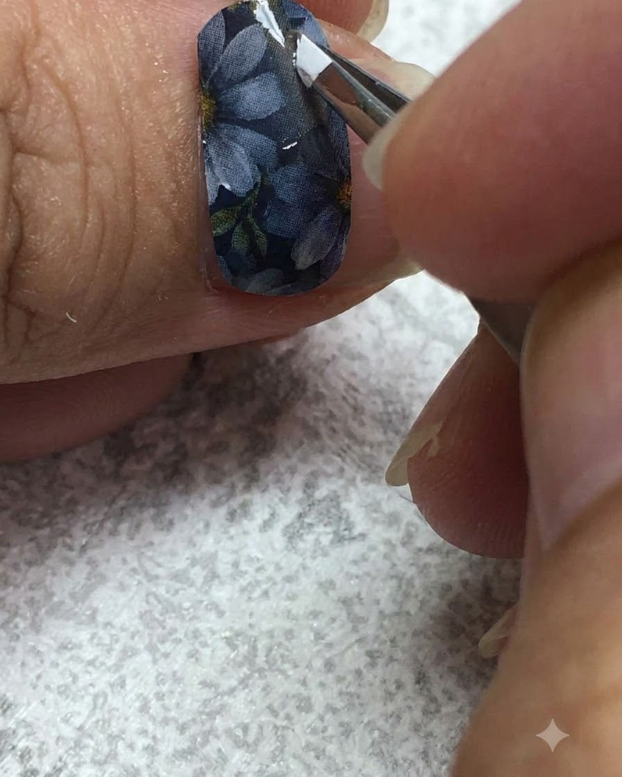 グレーのネイル上で、極細ライナーブラシを使ってデイジーの花びらに白いジェルを丁寧に描いている様子。