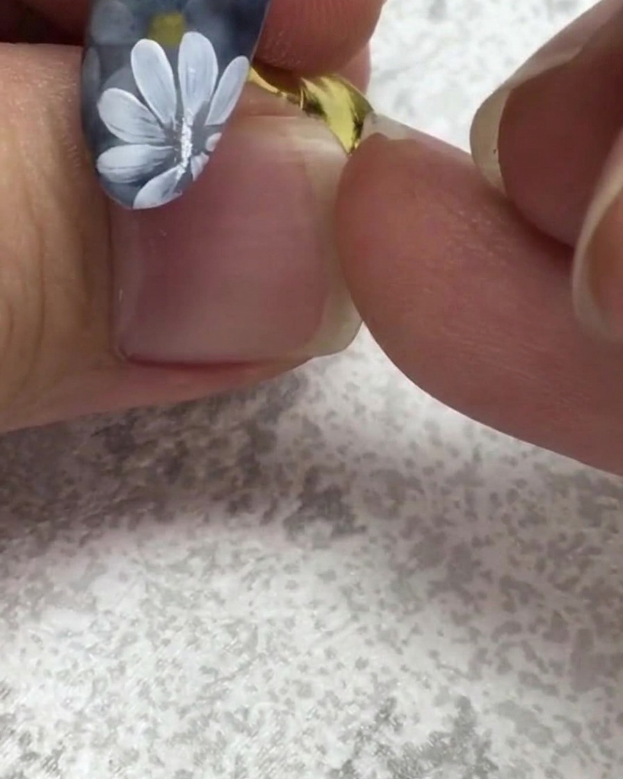 白いデイジーが描かれたネイルの近くで、フラットなネイルブラシが少量の緑色のジェルを取っている様子。
