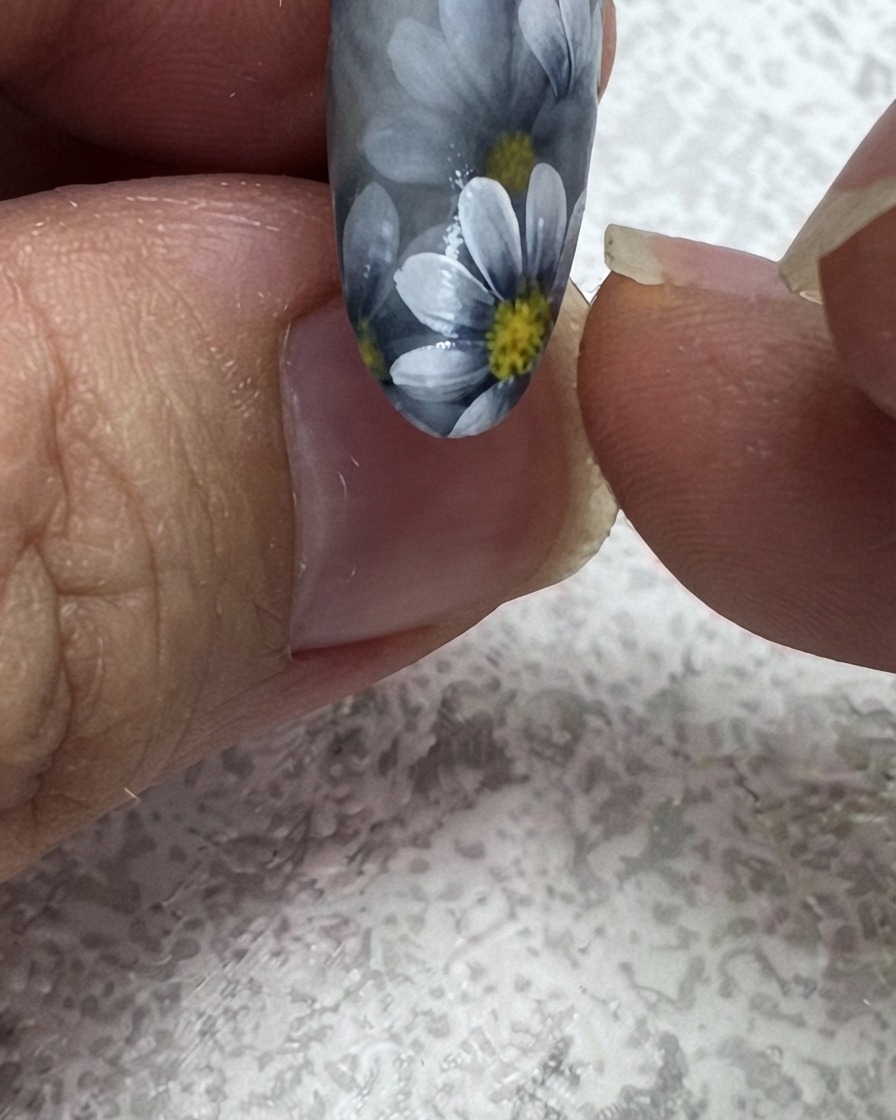極細ライナーブラシがフローラルネイルデザインの上隅に2枚目の緑の葉を加えている様子。