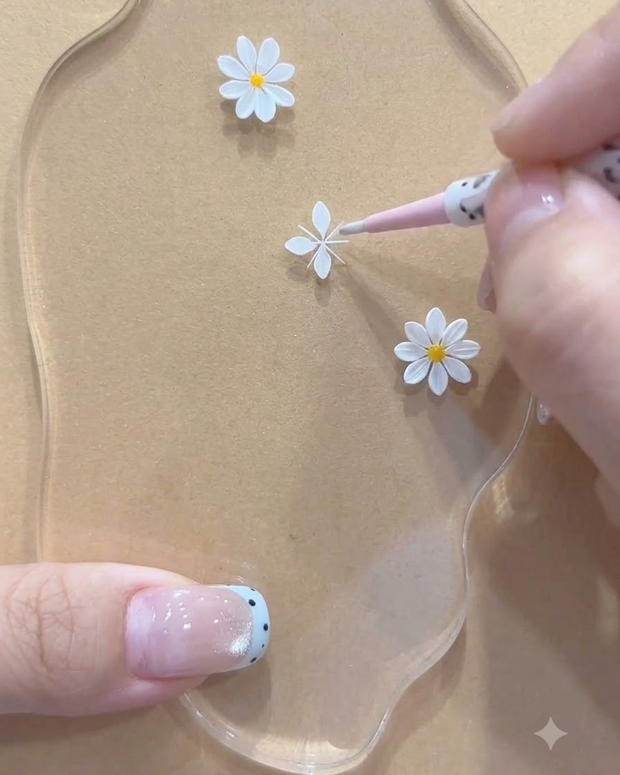 アクリルパレット上の小さなデイジー用に、白く描かれた花びらの構造を調整しているピンクのツールのクローズアップビュー。
