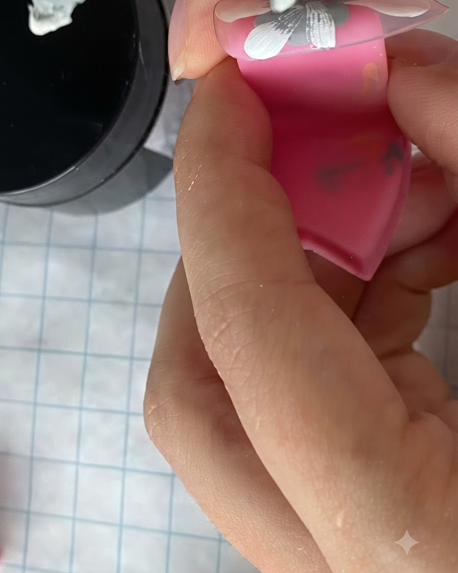 ピンクのスタンドに装着されたネイル全体に描かれた、白いデイジーの花びらの群れを細筆で塗りつぶしている様子。