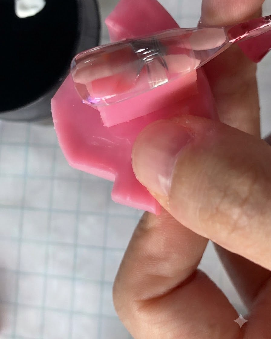 ネイル上の硬化されたデイジーフラワーのデザインの上に、小さなネイルブラシで半透明のピンクジェルを塗布している様子。