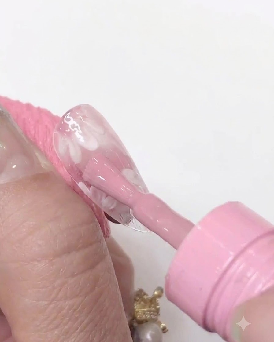 適用されたピンクのジェル層を硬化させるために、クリアネイルチップのすぐ近くにかざされたミニUV/LEDネイルランプ。