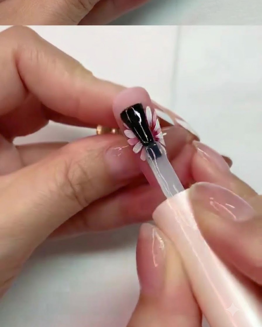ペイントされたデイジーネイルデザインの中央の花びらにマットトップコートを慎重に塗布しているブラシ。