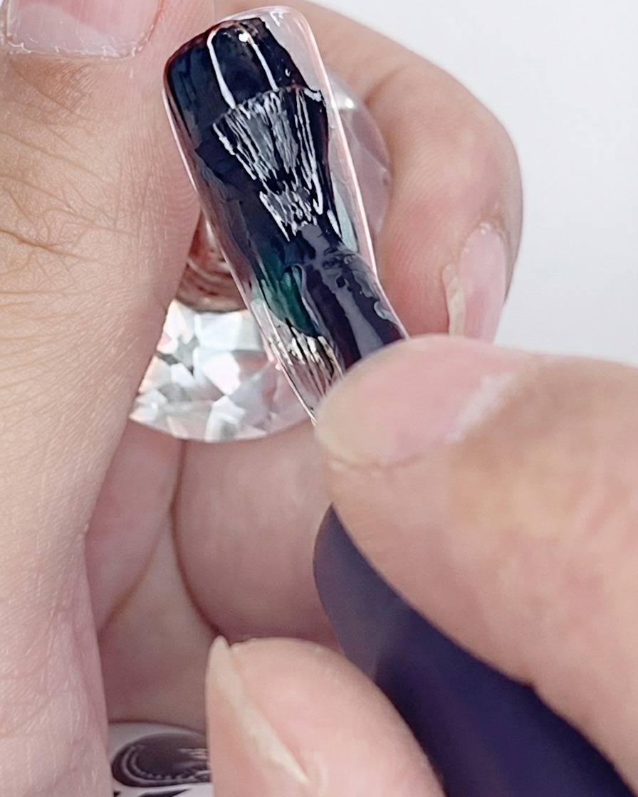 人工ネイルチップの上に黒ジェルポリッシュの1層目を塗っているブラシ。