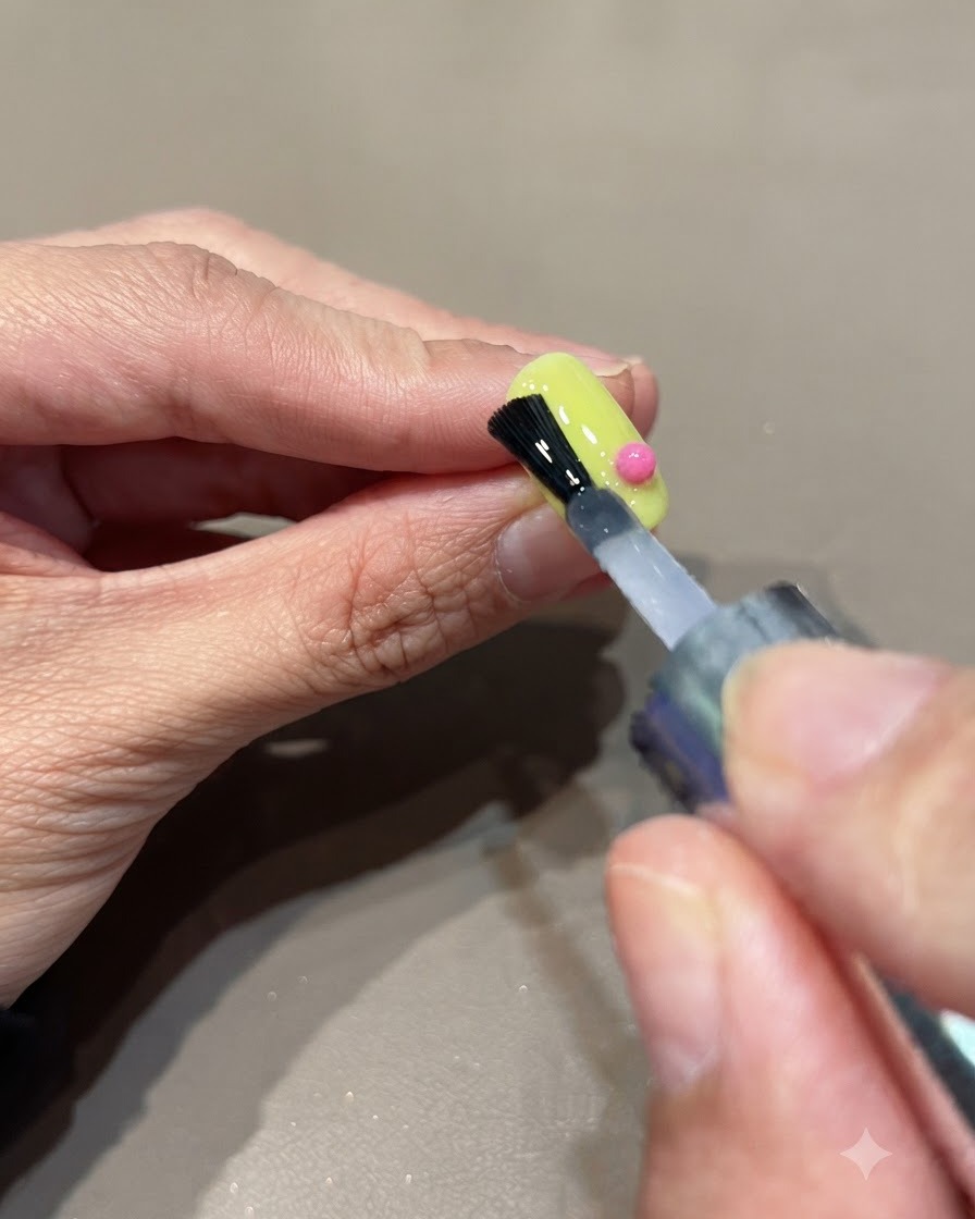 ミニハンディUVライトをネイルに近づけ、ピンクの球体の装飾があるネイル表面の接着剤を硬化させている様子。