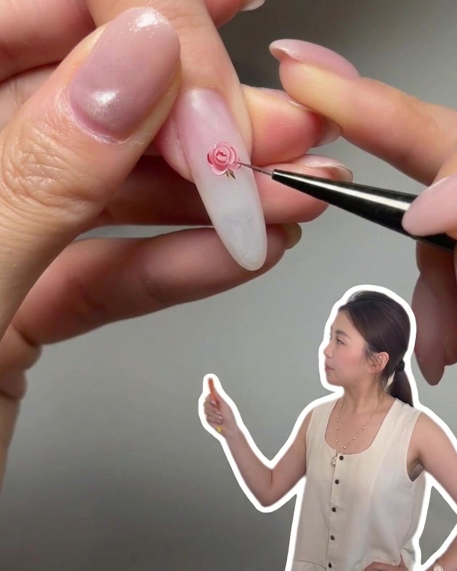 極細の筆を使ってアーモンドシェイプのネイルにピンクのジェルを塗り、チークネイルアートのデザインを作っているクローズアップ写真。