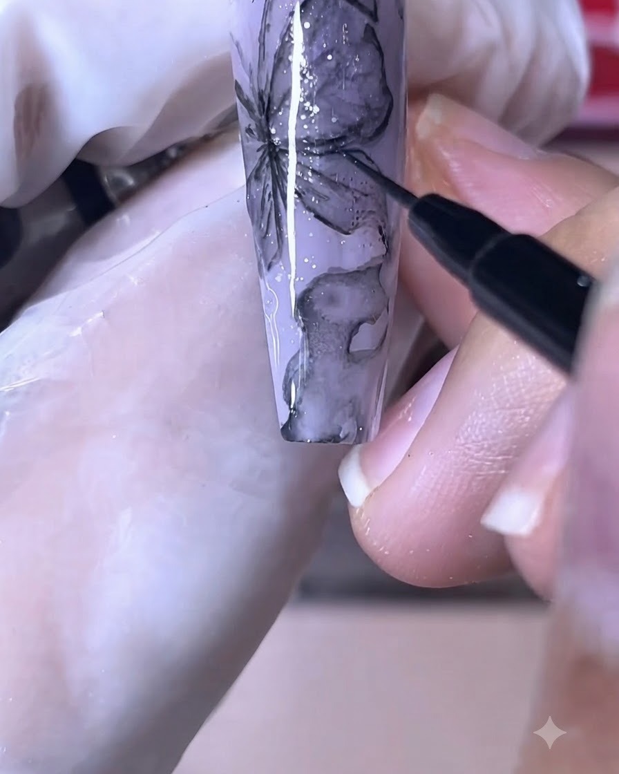 パープルバタフライのネイルデザインに、細いネイルブラシでくっきりとした黒い線を描いている様子。
