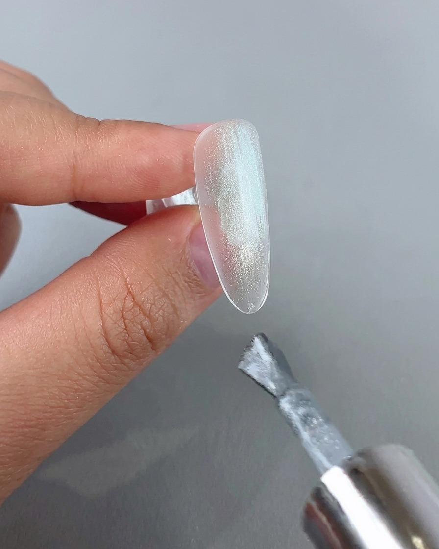 クリアなネイルチップに、シルバーの輝きを持つキャッツアイジェルを筆で塗布している様子。