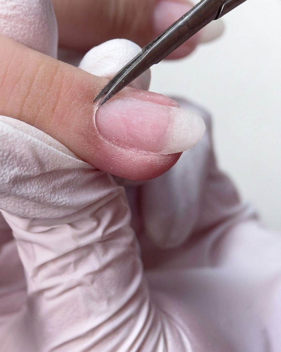 細いネイルシザーズで爪の根元から余分な古いキューティクル組織をきれいにカットしている様子。