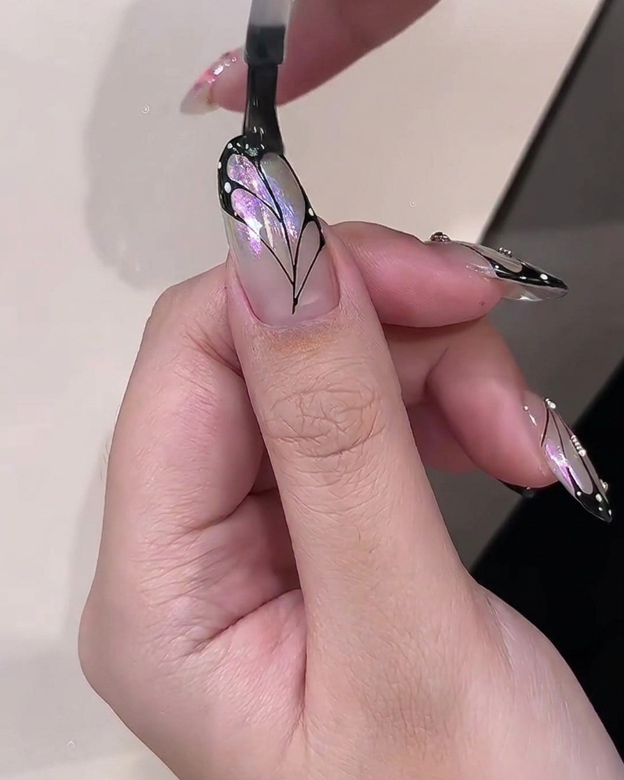 完成した蝶の羽のネイルアートのデザインの上に透明な光沢のあるトップコートを塗布しているブラシ。