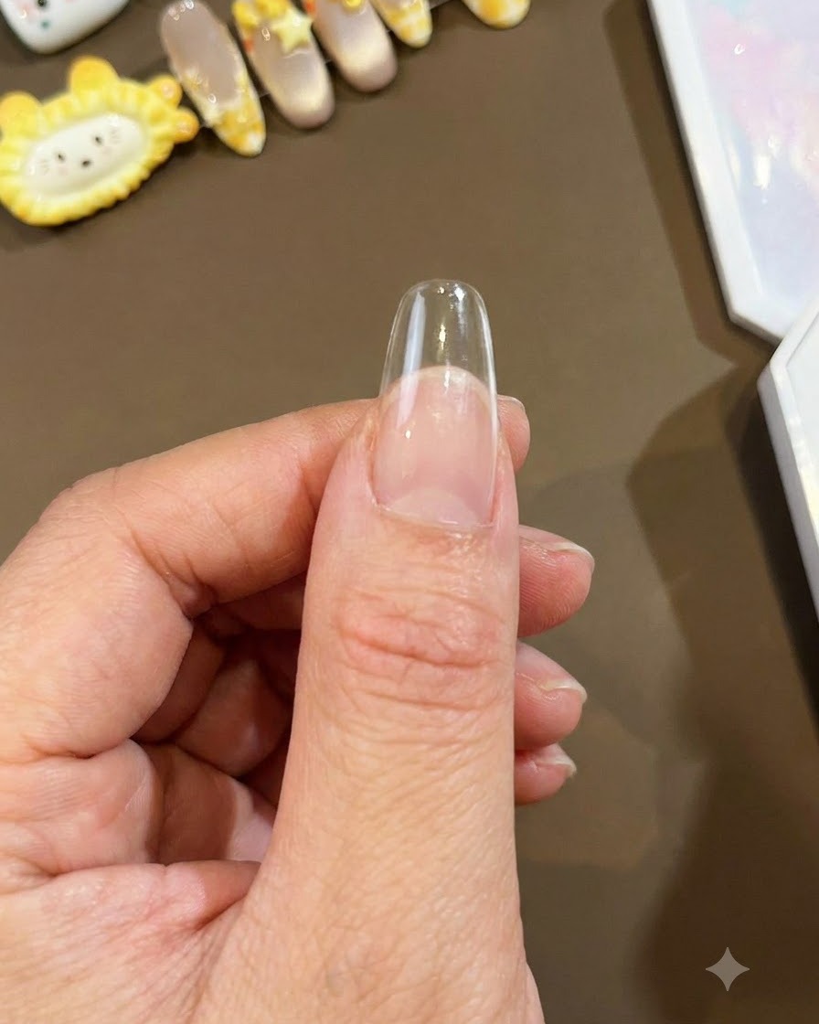 親指に固定されたクリアなロングアーモンド型のネイルチップのクローズアップ。アートの塗布に向けた準備が整っている状態。
