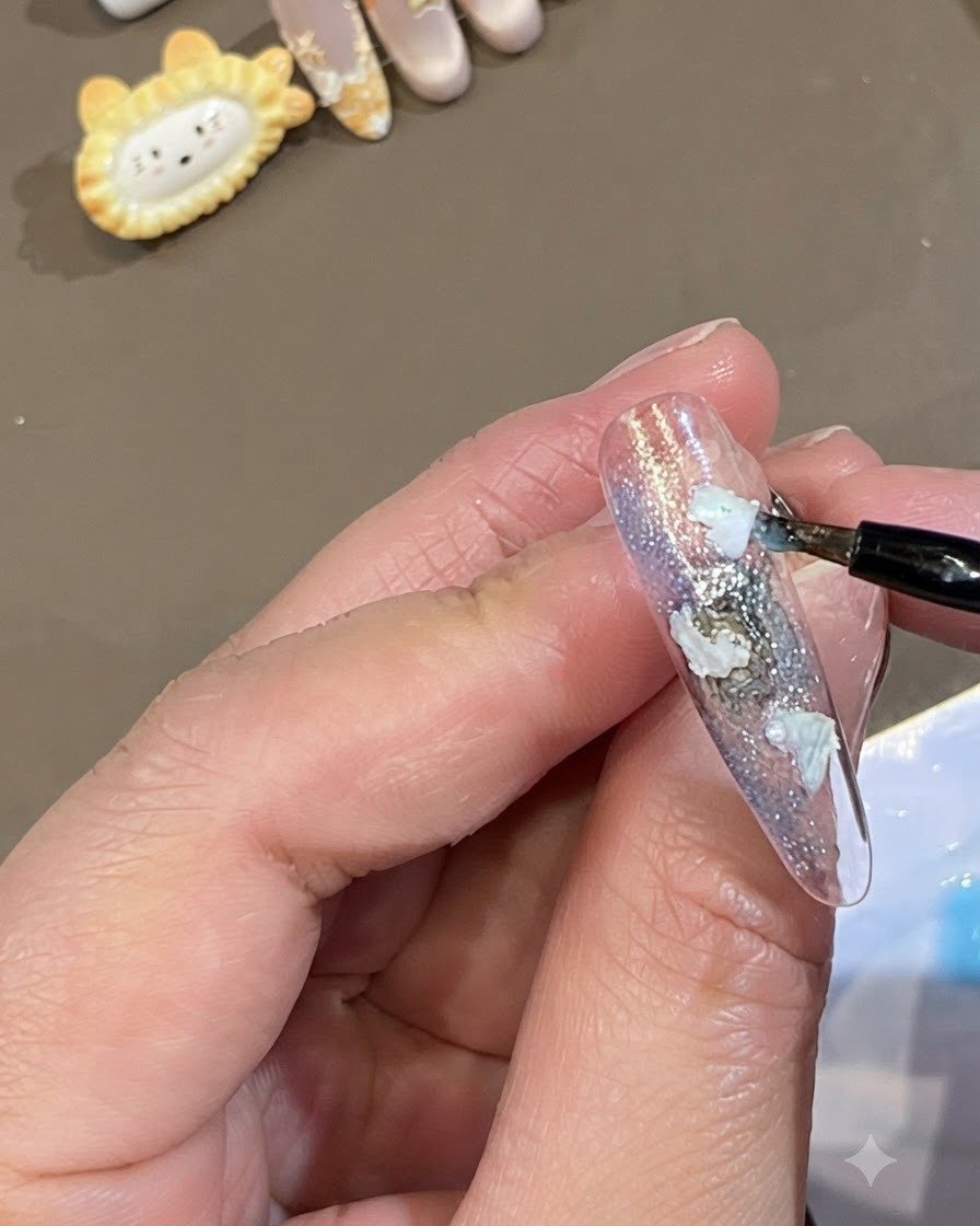 細いブラシを使い、ネイル上の白いシェル片のエッジに沿って半透明のブルーのジェルをドット状に置いているところ。