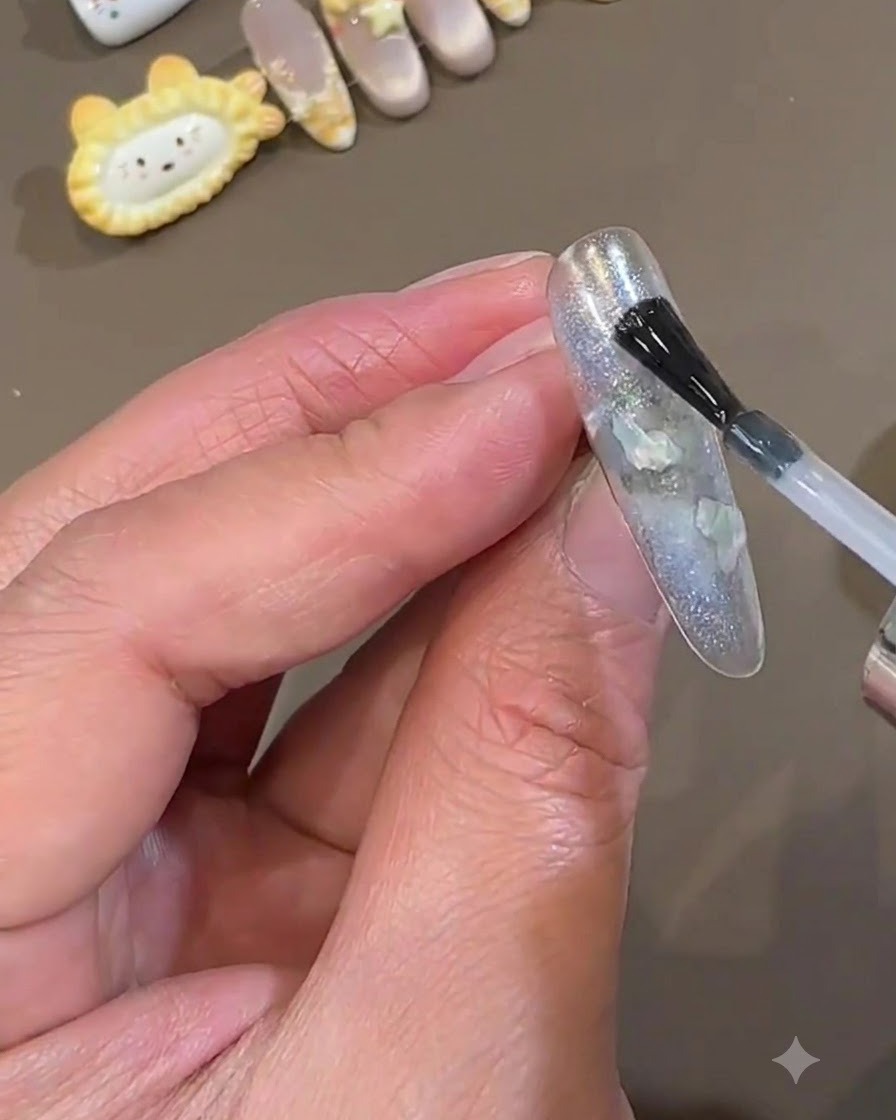 ポリッシュブラシを使い、アイスブルーのパーツを埋め込んだネイルの上に滑らかなクリアトップコートを塗っているところ。