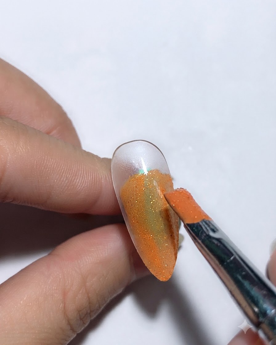 オレンジ色のネイルベースの上に、ブラシでスターリースカイグルーを塗っている様子。