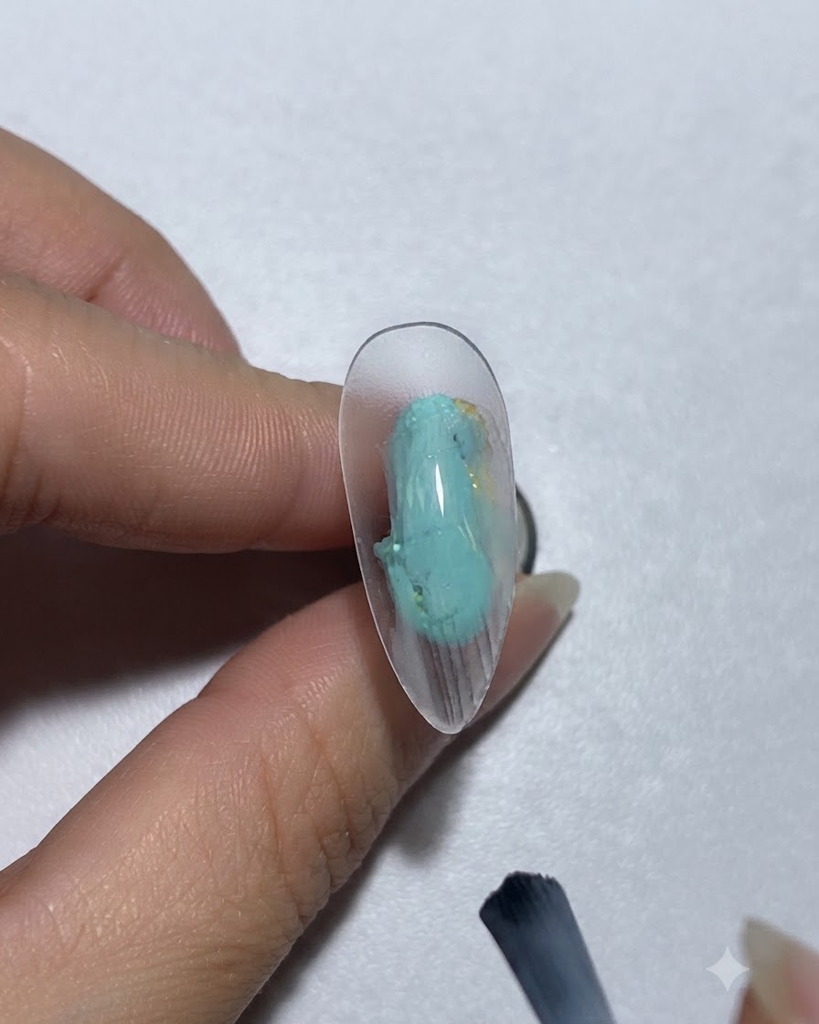 緑がかった青のペイントジェルをブラシで爪に塗布している様子。